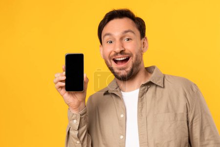 Un homme tient un téléphone portable devant son visage, se concentrant sur l'écran. Il semble être engagé avec l'appareil, montrant une belle application ou une offre en ligne