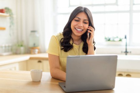 Eine Frau aus dem Nahen Osten macht Multitasking und telefoniert mit ihrem Handy, während sie an ihrem Laptop arbeitet. Sie wirkt konzentriert und in ein Gespräch verwickelt, während sie am Computer tippt.