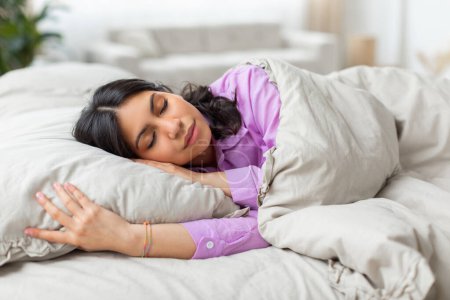 Eine Frau aus dem Nahen Osten liegt mit geschlossenen Augen im Bett. Sie wirkt entspannt und ausgeruht, möglicherweise schlafend oder meditierend. Der Fokus liegt auf ihrem friedlichen Ausdruck und ihrer Stille.