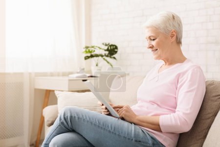 Foto de Sonriendo hermosa mujer mayor usando tableta digital en casa, espacio vacío - Imagen libre de derechos