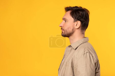 Foto de Un hombre está parado frente a un fondo amarillo brillante. Él está vestido casualmente y parece estar mirando hacia adelante, vista de perfil - Imagen libre de derechos
