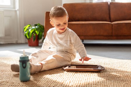 Un niño está sentado en el suelo, absorto en jugar con un dispositivo de tableta. Su enfoque está en la pantalla mientras interactúa con el contenido digital