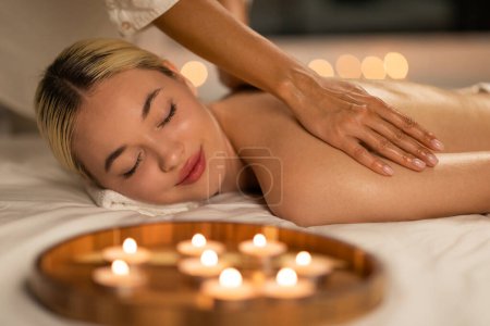 Téléchargez les photos : Une femme blonde s'allonge face contre terre tout en profitant d'un massage du dos apaisant dans un spa, son expression une de relaxation profonde et de confort. - en image libre de droit