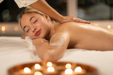 Eine junge Frau mit blonden Haaren genießt in einem ruhigen Wellnessbereich eine wohltuende Rückenmassage, die Entspannung und Ruhe betont.