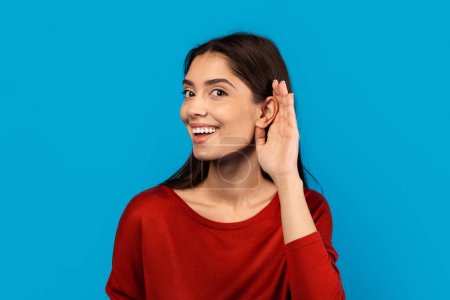 Eine Frau mit freudigem Gesichtsausdruck lächelt und berührt ihr Ohr mit der Hand, was darauf hindeutet, dass sie zuhören oder einen Ohrhörer anpassen könnte. Sie wirkt zufrieden und engagiert im Moment.