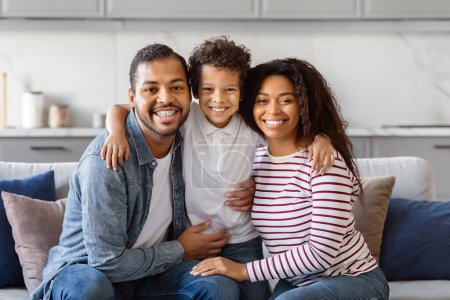 Happy African American family is seated on a comfortable couch. They seem to be engaged in conversation or watching TV together in a cozy living room setting.