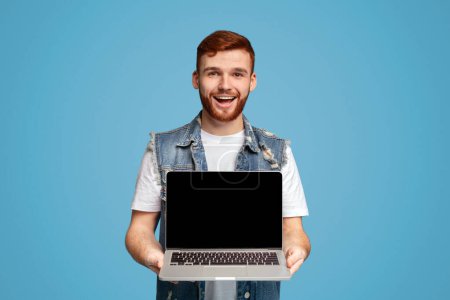 Happy millennial man showing to camera laptop with blank screen for mockup