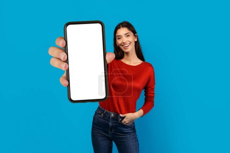 Foto de Una mujer con una camisa roja está sosteniendo un teléfono celular con la pantalla en blanco en la mano, la pantalla es visible. Ella parece estar interactuando con el dispositivo, posiblemente tomando una foto o enviando un mensaje. - Imagen libre de derechos