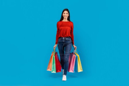 Una mujer con un suéter rojo de pie mientras sostiene las bolsas de la compra en sus manos. Parece estar al aire libre, posiblemente después de un viaje de compras..