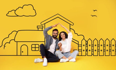 A cheerful multiethnic couple is sitting down with their hands raised to create the roof, expressing joy and togetherness. Behind them, a simple drawing of a house and a fence