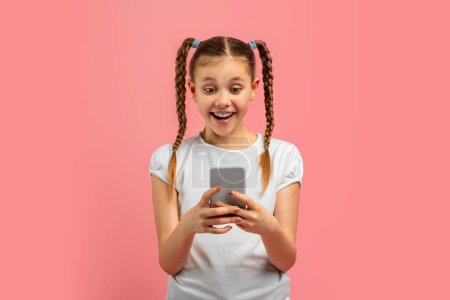 Téléchargez les photos : Jeune fille caucasienne exprimant son étonnement devant le contenu du smartphone, isolé sur fond rose avec une expression adolescente vibrante - en image libre de droit