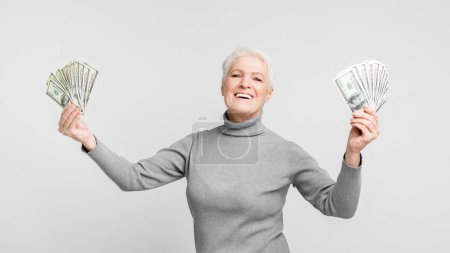 Photo for Joyful elderly European woman displaying both hands with money, signifying prosperity and enjoyment in s3niorlife - Royalty Free Image
