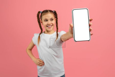 Téléchargez les photos : Adolescente joyeuse affichant avec confiance un écran de smartphone, isolée sur un fond rose, mettant l'accent sur la sagesse technologique des jeunes - en image libre de droit