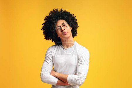 Skeptical black millennial man, looking suspiciously at camera with crossed hands, orange background