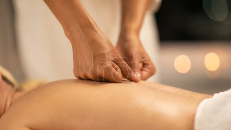 Eine Frau liegt mit dem Gesicht nach unten auf einem Massagetisch in einem Wellnessbereich, während eine Massagetherapeutin eine Rückenmassage durchführt. Die Hände der Therapeuten sind sichtbar, wenn sie Druck ausüben, Nahaufnahme