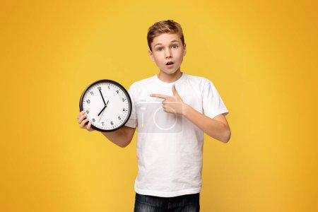 Young boy with a shocked expression pointing at a wall clock.