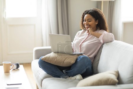 A content African American lady works from her cozy home environment, reflecting modern telecommuting practices