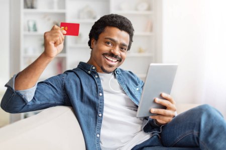 Black guy sitting at home with a credit card and tablet, representing online shopping and payment security