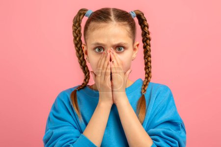 Una adolescente con el pelo trenzado cubre su boca en shock, mostrando una expresión facial sorprendida, sobre un fondo rosa