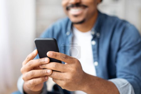 Téléchargez les photos : Vue détaillée d'un homme afro-américain manœuvrant un smartphone, mettant en évidence notre connexion à la technologie dans la vie quotidienne - en image libre de droit