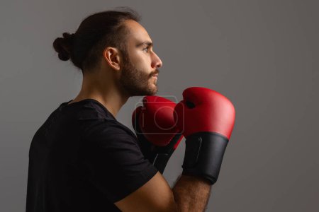Zu sehen ist ein Mann in schwarzem Hemd mit roten Boxhandschuhen, bereit für einen Boxkampf oder eine Trainingseinheit. Er wirkt fokussiert und entschlossen und zeigt seine körperliche Stärke und Beweglichkeit.