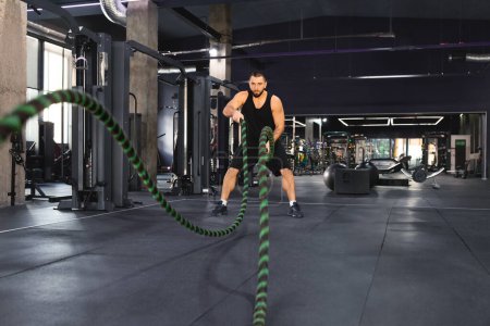 A man is working out in a gym, holding a rope and engaging in various exercises to strengthen his upper body and core muscles, focused and determined on the intense workout routine.