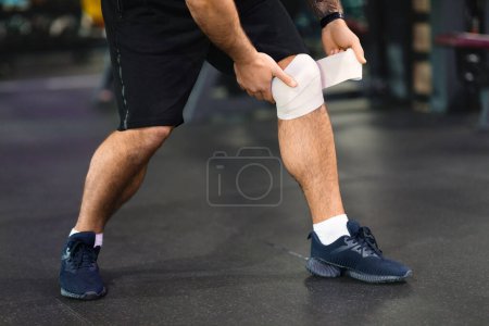 Cropped of man is shown with a bandage wrapped securely around his injured leg. He appears to have workout at gym
