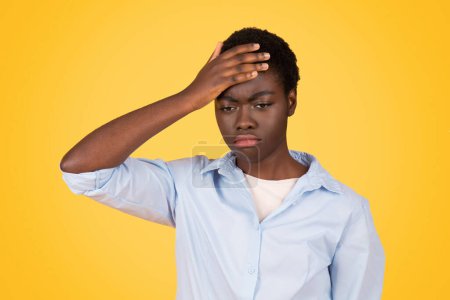 Femme afro-américaine affiche un geste de souffrance, son expression évoquant les défis qui peuvent être confrontés à un zoomer isolé sur fond jaune
