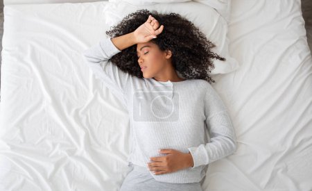 Photo for A young Hispanic woman in a tranquil state of sleep, lying comfortably in a bed adorned with white linens. Her pose suggests a deep and restful slumber, with one arm resting gently on her forehead - Royalty Free Image