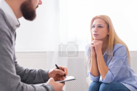 Photo for A young woman sits thoughtfully, her chin resting on her hand, engaged in a conversation with a man therapist who is taking notes - Royalty Free Image