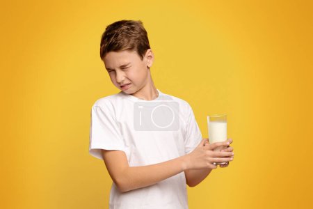 Laktoseintoleranz. Netter kleiner Junge will keine Milch trinken und runzelt die Stirn auf orangefarbenem Hintergrund