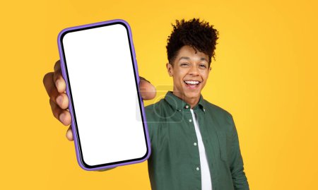 Jeune homme brésilien élégant est vu tenant un téléphone cellulaire dans sa main, se concentrant sur l'écran des appareils avec une expression sérieuse. Le fond est flou, mettant l'accent sur l'homme et le téléphone.