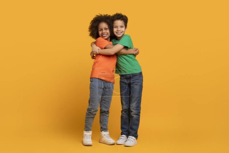 Two young African American children are embracing each other in a warm hug on a bright yellow background.
