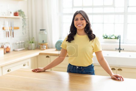 Téléchargez les photos : Une femme du Moyen-Orient avec une chemise jaune est debout à un comptoir de cuisine, se livrant à des activités ménagères. Elle semble concentrée et occupée pendant qu'elle prépare la nourriture ou nettoie la cuisine. - en image libre de droit