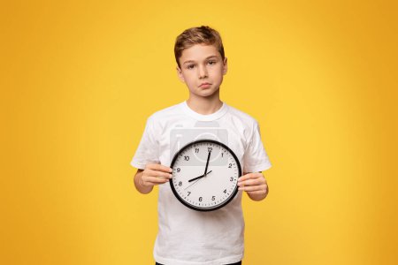 Téléchargez les photos : Concept de temps de quarantaine. bouleversé adolescent garçon tenant Gros horloge orange studio fond - en image libre de droit