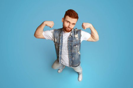 Awesome strong caucasian man showing his power and biceps on blue background