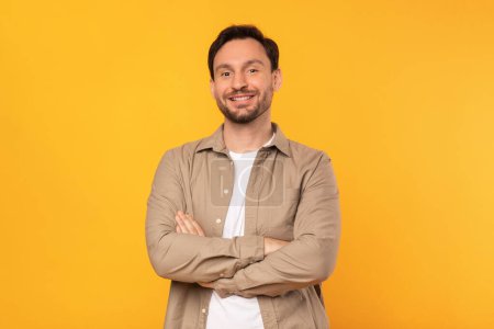 Photo for A man is standing confidently with his arms crossed in front of a bright yellow background, displaying a posture of strength and determination - Royalty Free Image