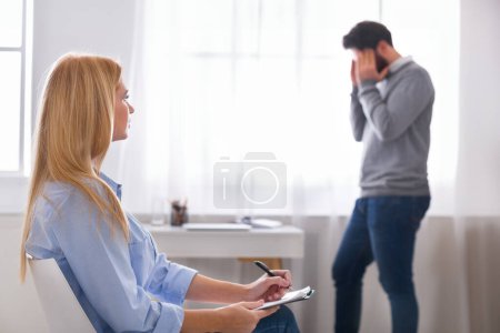 Photo for Depressed man emotionally speaking at psychotherapist session, walking in doctors office, specialist making notes or filling in his personal information - Royalty Free Image