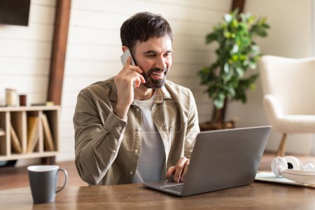 Photo for A man is multitasking by talking on a cell phone and using a laptop simultaneously. He appears focused on his work, balancing communication and productivity on two devices. - Royalty Free Image