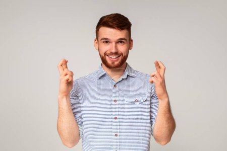 Foto de Positivo millennial chico cruzando los dedos y pidiendo deseo sobre fondo beige, panorama - Imagen libre de derechos