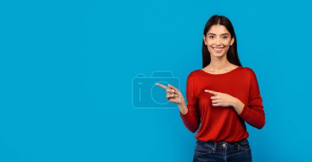 Photo for A woman wearing a red sweater is pointing at an unseen object off-camera, engaged and focused on whatever has caught her attention, her gesture suggesting significance or direction, copy space - Royalty Free Image