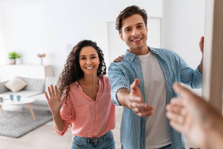 Photo for Portrait of cheerful couple inviting guests to enter home, happy young guy and lady standing in doorway of modern flat, looking out, man shaking hands, meeting new neighbors or friends - Royalty Free Image