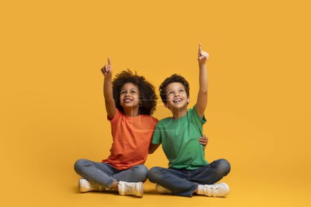 Photo for Two African American young children, sitting on the floor, have their arms lifted into the air. They appear to be engaged in a playful or celebratory activity, showing their excitement and enthusiasm. - Royalty Free Image