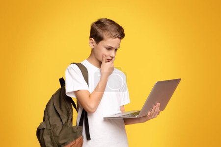 Téléchargez les photos : Un jeune garçon portant un sac à dos et travaillant sur un ordinateur portable à l'extérieur. - en image libre de droit