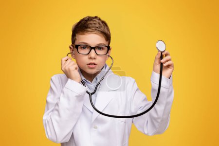 Photo for Actual game. Little boy in medical uniform playing with stethoscope, orange panorama background with free space - Royalty Free Image