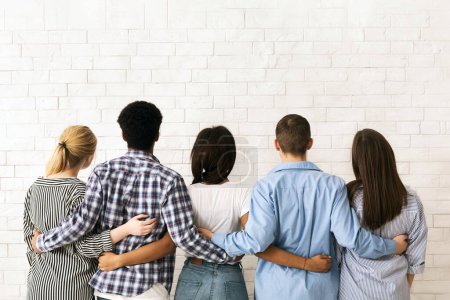 Eine Gruppe multiethnischer Teenager steht dicht mit dem Rücken zum Betrachter, die Arme umeinander in einem Zeichen der Freundschaft und Einheit, Rückansicht