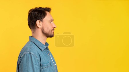 Téléchargez les photos : Un homme est représenté debout devant un fond jaune solide. Il semble regarder directement l'espace de copie, panorama - en image libre de droit