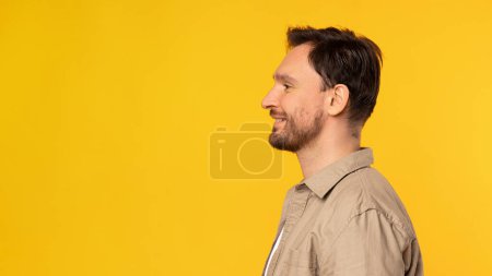 Ein Mann steht aufrecht vor leuchtend gelbem Hintergrund. Er sitzt zentral im Rahmen und trägt lässige Kleidung, Seitenansicht