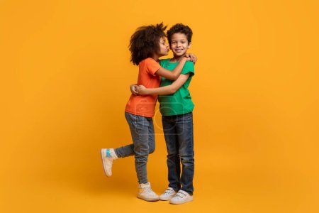 Foto de Dos niños afroamericanos se abrazan calurosamente sobre un fondo amarillo brillante. Sus rostros muestran alegría y afecto mientras comparten un abrazo sincero. - Imagen libre de derechos