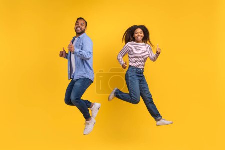 African American man and woman are captured mid-air as they jump energetically, displaying a moment of joy and freedom, yellow background